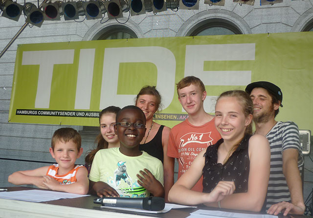 Eine Gruppe aus Kindern und Jugendlichen steht vor dem TIDE Logo
