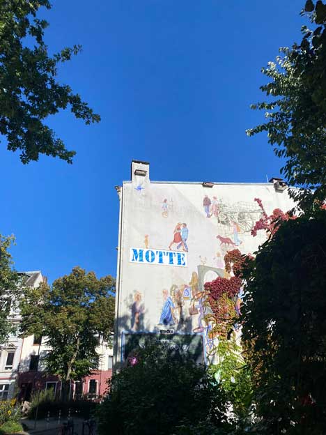 Hauswand mit Malerei, Schriftzug Motte, blauer Himmel.