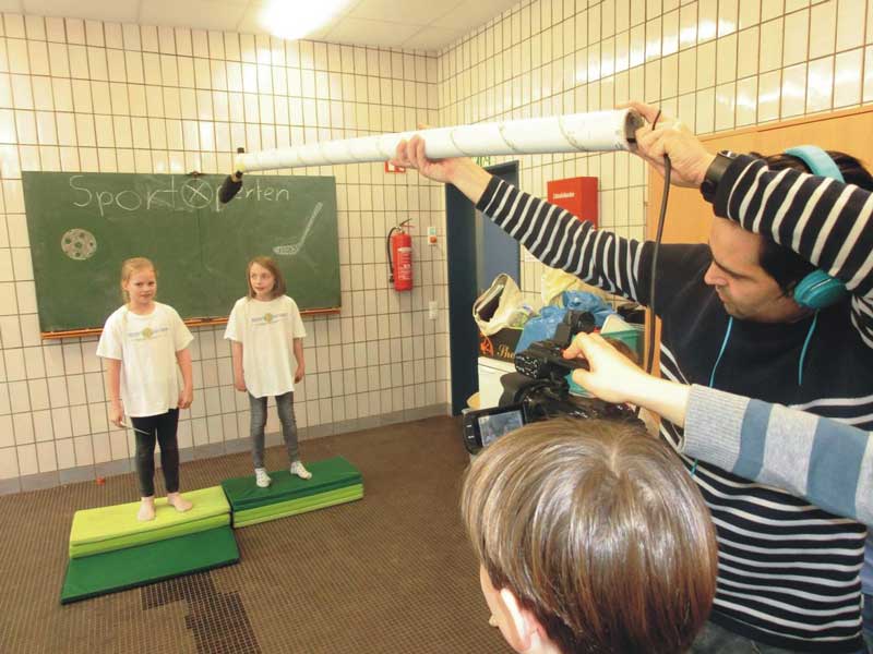 Kinder stehen vor Tafel, Mikrofonangel wird ins Bild gehalten