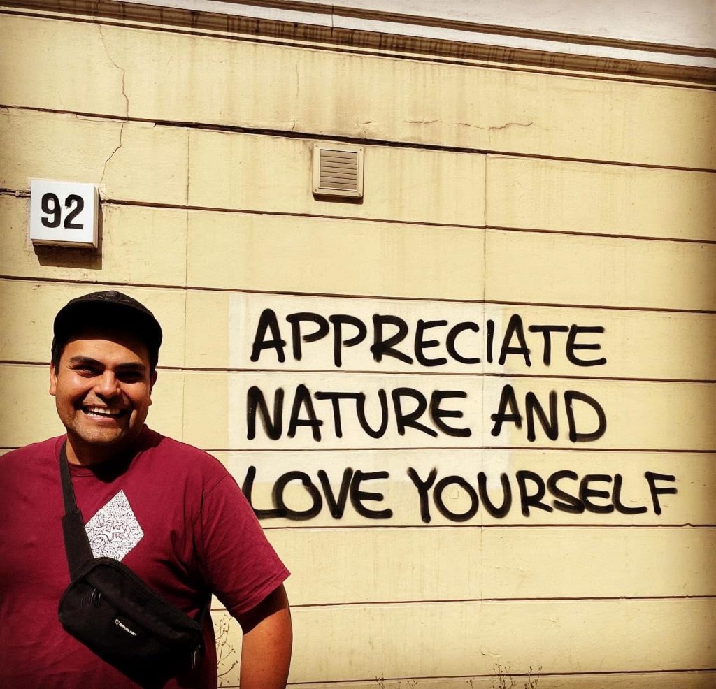 Person in rotem Shirt vor Hauswand mit Grafitty Appreciate Nature and Love yourself